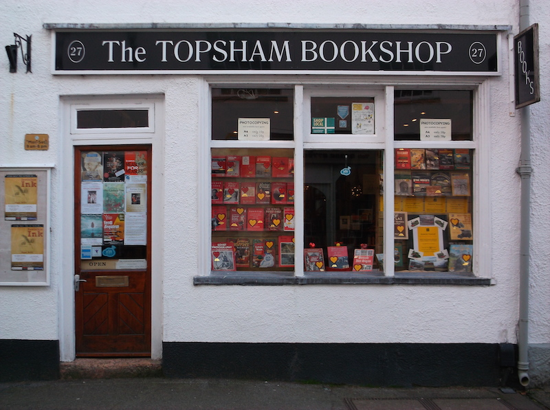 An interior room at The Topsham Bookshop with painted shelving and a lower section piled with books.